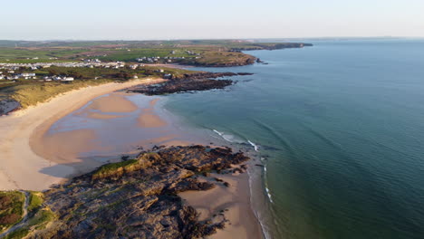 Aerial-shot-of-the-blue-sea,-rocks,-beach-and-fields-in-Cornwall,-UK