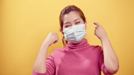 Young-Asian-woman-is-happy-and-smiling-and-taking-off-the-protective-mask-for-fresh-air-after-the-CIVID-19-situation-unravels-with-the-yellow-background