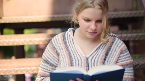 Close-up-of-a-girl-student-turning-a-page-while-reading-a-book-outside-on-stairs