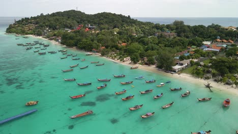 Slow-flyover-shot-of-a-boat-filled-beach-on-Ko-Lipe-Island,-Thailand-on-a-bright-clear-day