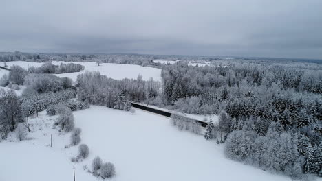 Aerial-drone-forward-moving-shot-over-narrow-highway-road-across-white-snow-covered-landscape-on-a-cloudy-day