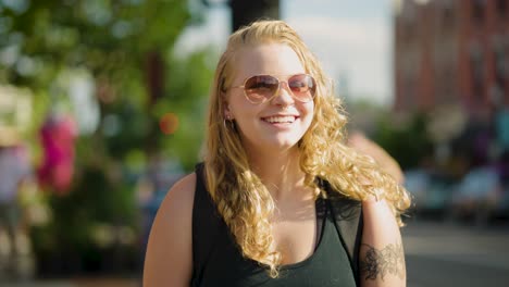 Girl-with-sunglasses-smiles-at-the-camera-while-walking-through-a-crosswalk-downtown