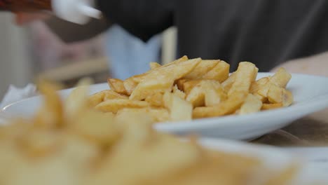 Gießen-Sie-Mit-Der-Hand-Salz-Und-Essig-Auf-Britische-Chips,-Bevor-Sie-Mittags-In-Der-Nähe-Essen