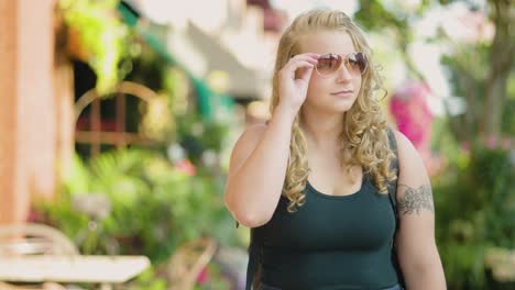 Girl-walks-on-the-sidewalk-downtown-and-adjusts-sun-glasses