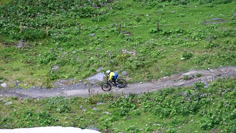 Two-bikers-are-riding-downhill-on-a-dirt-sinuous-track-with-helmet-and-protections,-swiss-alps,-Obwalden,-drone-aerial-view