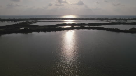 Aerial-view-in-forward-flight-of-fishing-ponds-by-the-sea,-mirror-silhouette,-slow-motion-1