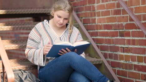 Studentin,-Die-Draußen-Auf-Der-Treppe-Ein-Buch-Liest,-Blättert-Eine-Seite-Ihres-Lehrbuchs-Um