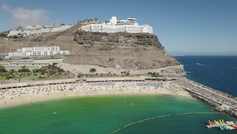 Circular-aerial-view-of-Playa-de-los-Amadores-in-Puerto-Rico,-Gran-Canaria-with-hotels-and-people-bathing-in-the-background-at-midday