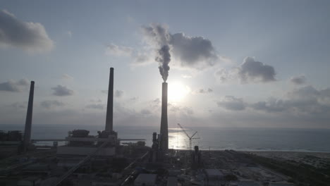 Aerial-view-of-a-power-plant-with-4-chimneys,-one-of-which-emits-thick-smoke-into-the-air,-polluting-energy-in-Israel