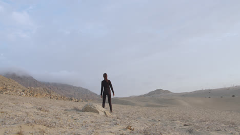 Long-shot-of-a-beautiful-woman-in-black-standing-next-to-a-rock-in-the-middle-of-the-desert-in-daylight