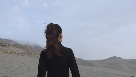 Beautiful-woman-from-behind-dressed-in-black-standing-in-the-cloudy-desert-in-the-afternoon-while-the-wind-blows-and-moves-her-hair