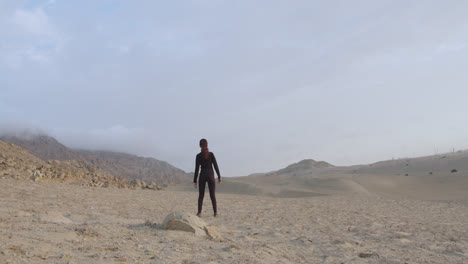Mysterious-woman-in-black-standing-next-to-a-rock-in-the-middle-of-the-desert-in-the-afternoon-light