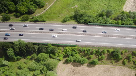Aerial-top-down-shot-of-traffic-on-asphalt-highway-surrounded-by-forest-trees-and-fields-in-summer
