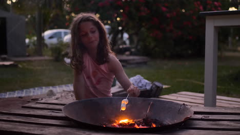 Cute-young-girl-toasting-marshmallows-on-a-skewer-over-a-fire