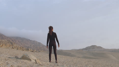 Cinematic-shot-from-behind-of-a-woman-in-black-observing-the-desert-with-a-cloudy-sky