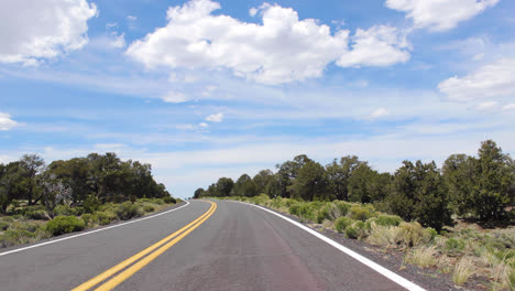 Slow-motion-pov-shot-from-a-car-driving-down-a-windy-country-road-in-Flagstaff-Ariozna-on-a-sunny-day-with-clouds-overhead