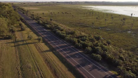 Drohne-Pov-Eines-Isolierten-Weißen-Autos,-Das-Entlang-Der-Geradlinigen-Ländlichen-Landstraße-Von-Uruguay-In-Der-Nähe-Der-Schwarzen-Lagune-Fährt