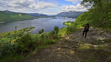 Woman-female-taking-a-photograph-on-a-mobile-phone-View-across-Derwentwater-in-the-English-Lake-District-looking-towards-the-town-of-Keswick-with-Skiddaw