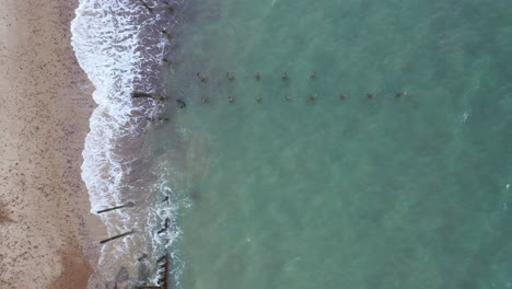 Aerial-top-down-footage-from-sea-defences-in-the-sea-towards-the-beach-with-waves-crashing-onto-the-beach