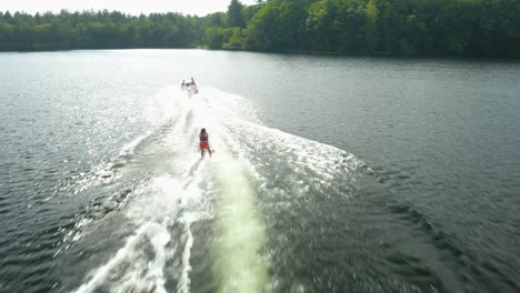 Outdoor-shot-of-a-woman-water-skiing-outside-in-a-blue-lake-With-many-luscious,-green-trees-in-the-background-and-a-cloudy-sky,-a-splash-of-water-or-waves-can-be-observed