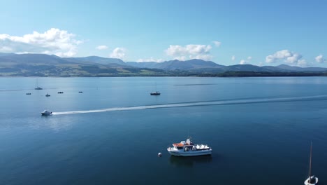 Speedboat-travelling-across-Snowdonia-clear-mountain-range-aerial-view-sunny-calm-Welsh-shimmering-seascape