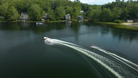 An-outdoor-shot-of-a-man-water-skiing-at-a-clear-lake-can-be-seen-with-many-lush,-green-trees-in-the-background,-partly-overcast-with-light-thunderclouds