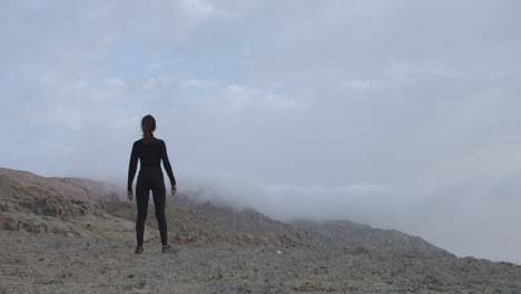 Long-shot-of-a-woman-from-behind-wearing-black-clothing-in-a-desert-at-dawn
