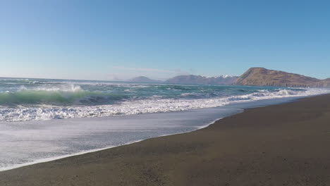 A-beautiful,-sunny-day-with-clear-blue-skies-along-a-sandy-beach-with-mountains-in-the-distance-on-Kodiak-Island-Alaska