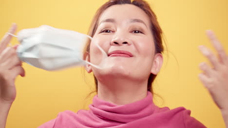 Close-up-Asian-woman-smiling-and-taking-off-the-protective-mask-for-fresh-air-after-the-CIVID-19-situation-unravels-with-the-yellow-background