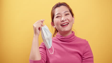 Asian-gorgeous-young-woman-smiling-and-taking-off-the-protective-mask-for-fresh-air-after-the-CIVID-19-situation-unravels-with-the-yellow-background