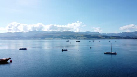 Snowdonia-clear-mountain-range-aerial-view-through-boats-on-sunny-calm-Welsh-shimmering-seascape