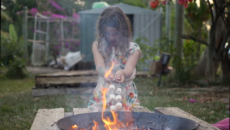 Young-girl-roasting-marshmallows-on-metal-sticks-over-backyard-fire