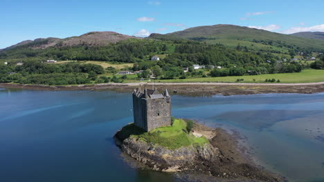 Impressive-drone-shot-of-Castle-Stalker,-Scotland,-sweeping-around-the-castle-from-above-on-a-spectacular-summer-day