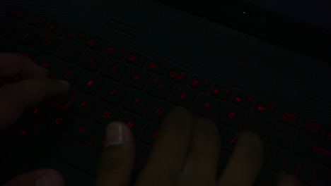 Draufsicht-Der-Hand,-Die-Auf-Der-Tastatur-Mit-Roter-Beleuchtung-Des-Laptops-In-Einem-Dunklen-Raum-Tippt,-Nahaufnahme