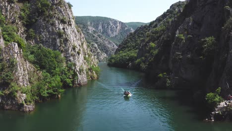 Small-boat-with-tourists-sails-between-the-steep-mountain-sides-over-Lake-Matka-in-the-major-tourist-attraction-Matka-Gorge-of-northern-marcedonia-on-a-sunny-summer-day
