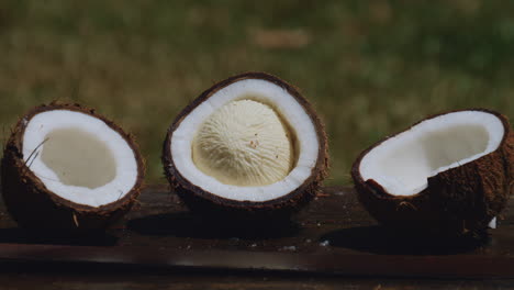 Zoom-out-from-three-halves-of-coconut-on-wooden-table,-one-in-midst-of-germination-process