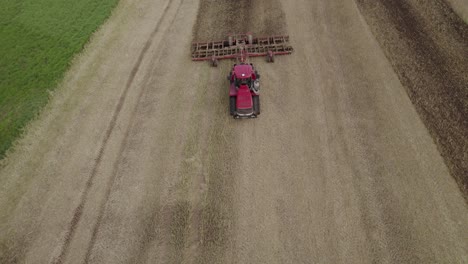 Aerial-shot-over-the-big-tractor-on-tracks-pulling-harrow-system-to-recultivate-soil-after-the-harvest---flying-backward