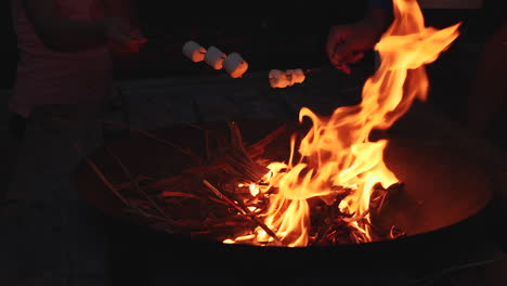 Slow-motion-close-up-of-dad-and-daughter-roasting-marshmallows-over-campfire-at-night
