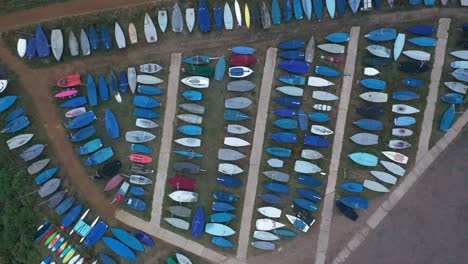 Rising-aerial-footage-revealing-yachts,-boats,-kayaks-and-dinghys-in-a-boat-yard-beside-an-estuary-in-Norfolk,-England
