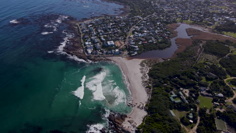 Aerial-view-of-holiday-town-Onrus-and-lagoon-as-waves-crash-onto-beach
