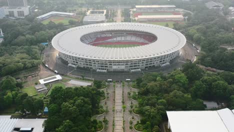 Aerial-zoom-in-of-GBK-Stadium-surrounded-by-sports-complex-at-sunset-in-Jakarta,-aerial