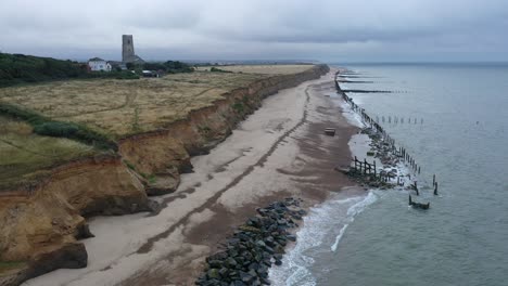 Slow-moving-aerial-footage-along-the-tide-coming-in-onto-sea-defences-towards-church