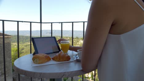 Young-female-entrepreneur-working-while-eating-her-breakfast-on-the-hotel-balcony