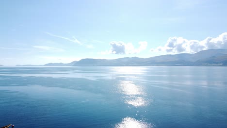 Shimmering-brilliant-blue-ocean-with-scenic-Snowdonia-mountains-across-the-horizon-aerial-view