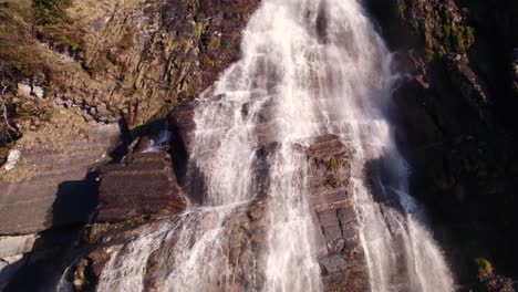 Aerial-drone-footage-raising-down-a-picturesque-waterfall-in-springtime-with-colorful-light-reflections-at-Fallbach-in-Grindelwald-in-Switzerland