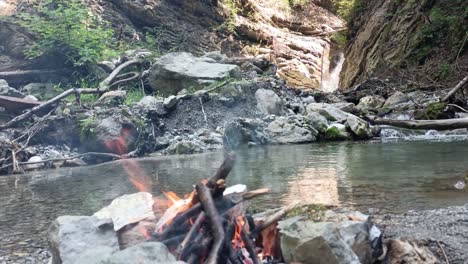 Bonfire-is-burning-in-nature-with-no-people-with-waterfall-and-river-in-background