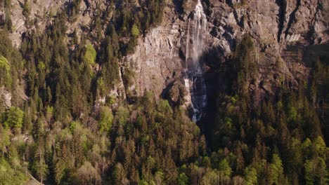 Aerial-drone-footage-raising-up-from-a-distance-with-stunning-views-of-Fallbach,-a-stunning-waterfall-in-Grindelwald,-Switzerland