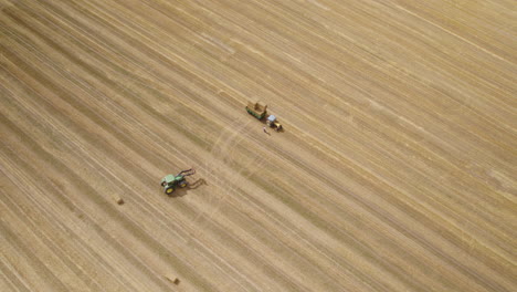 Aerial-top-down-shot-of-tractor-loading-rolled-hay-bales-on-trailer-hanger-at-wheat-field