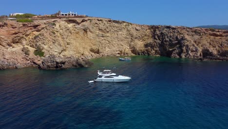 White-luxury-yacht-in-bay-on-cliff-villa-Buttery-soft-aerial-view-flight-fly-backwards-drone-footage-of-cliff-edge-beach-Sa-Figuera-borda-Ibiza-summer-2022-Philipp-Marnitz-4k-Cinematic-view-from-above