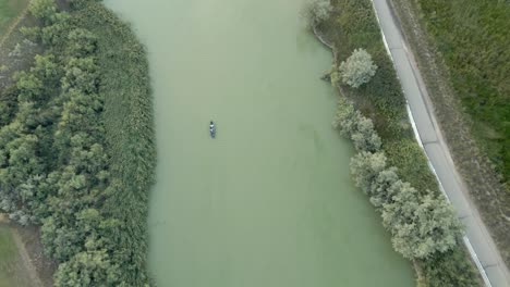 Small-motorboat-going-down-a-green-river---straight-down-aerial-view